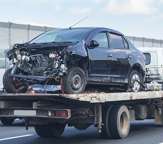 A heavily damaged black car being towed on a flatbed truck