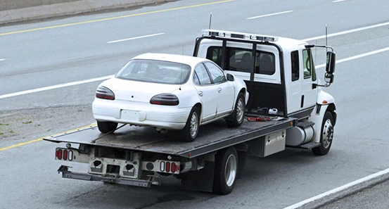 A white tow truck on a highway, towing a white sedan