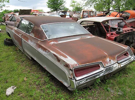 A heavily rusted, abandoned 1960s Dodge Polara in a junkyard