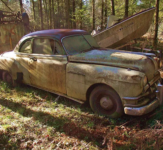 A heavily rusted, abandoned 1950 Pontiac Chieftain in a forest