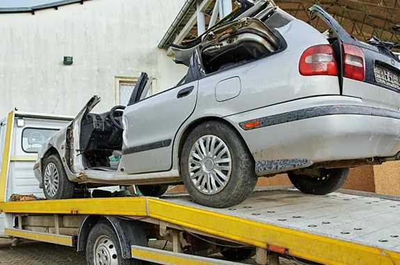 A damaged, silver car being towed on a flatbed truck